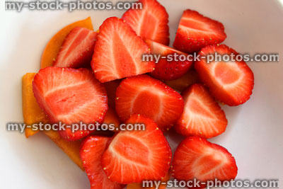 Stock image of cut strawberries in dish with persimmon fruit pieces, healthy dessert
