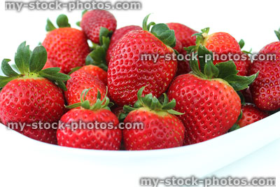 Stock image of fresh red strawberries, strawberry fruit / green stalks, white dish