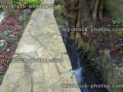 Stock image of crazy paving pathway in landscape garden, by stream