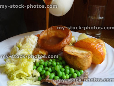 Stock image of Sunday roast dinner, beef, Yorkshire pudding, pouring gravy, roast potatoes, vegetables, carrots peas cabbage cauliflower stuffing