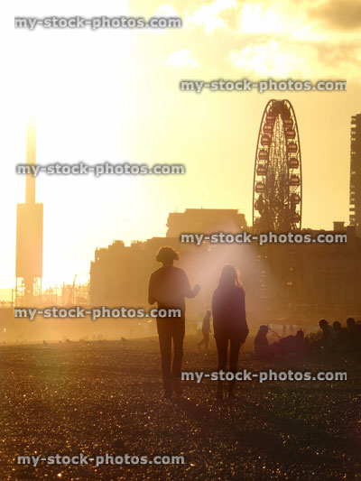 Stock image of couple walking on Brighton beach, sunset with big wheel