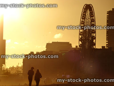 Stock image of couple walking on beach at sunset time, big wheel