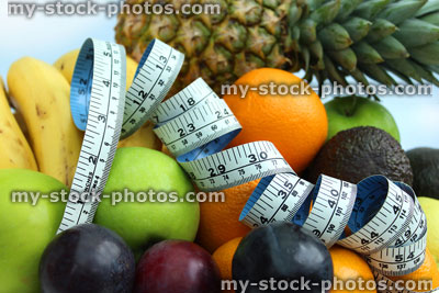 Stock image of tape measure with bananas, apples, oranges, pineapple, plums, avocado, satsumas