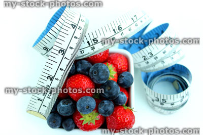 Stock image of tape measure with fresh organic strawberries and blueberries