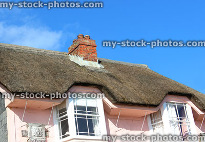 Stock image of thatched roof with brick chimney, pink cottage, white bay windows