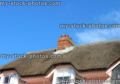 Stock image of traditional thatched cottage with pink walls, chimney pots