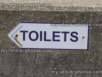 Stock image of white arrow sign on wall, pointing to 'toilets'