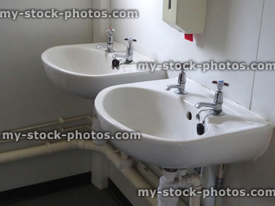 Stock image of two dirty white ceramic sinks in public toilet