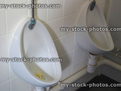 Stock image of two white urinals in a men's public toilets / restroom, tiled wall