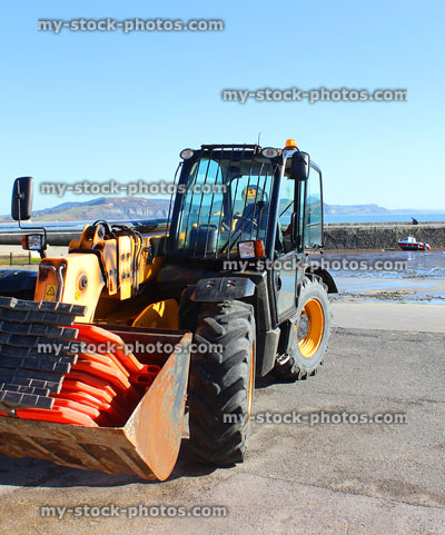 Stock image of tractor by harbour walls, tide out with muddy beach