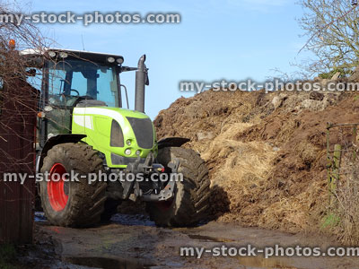 Stock image of green tractor on farm, pile of manure, muck spreading
