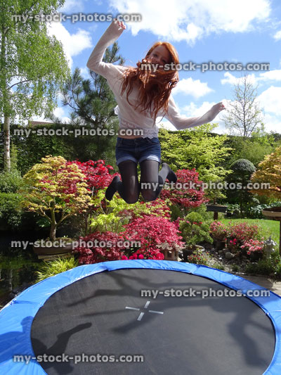 Stock image of girl playing outside in garden, bouncing on trampoline