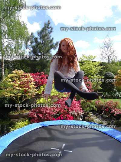 Stock image of girl sitting in mid air, bouncing on trampoline in garden