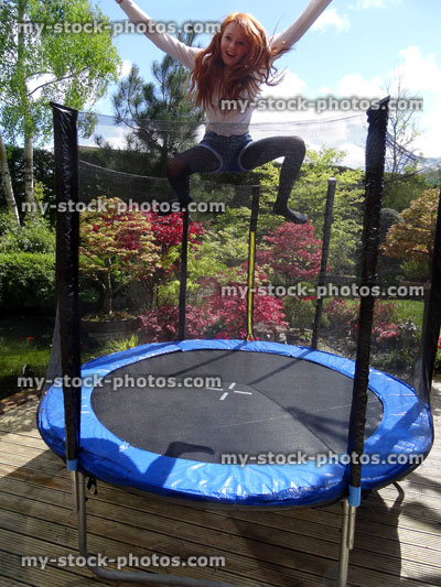 Stock image of girl bouncing on trampoline in sunny garden, with safety net
