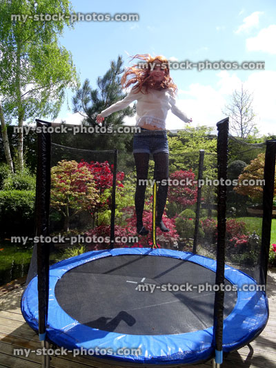 Stock image of girl playing in garden, bouncing on round trampoline