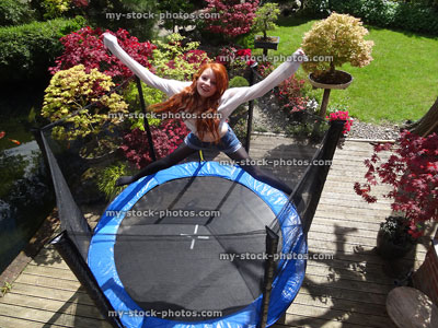 Stock image of girl jumping high, bouncing on trampoline, above safety net