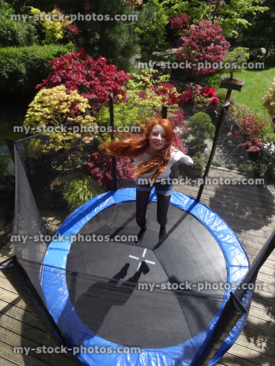 Stock image of girl on round trampoline in landscaped garden, bouncing