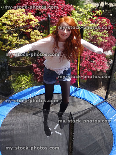 Stock image of pretty girl bouncing high on garden trampoline, over safety net 