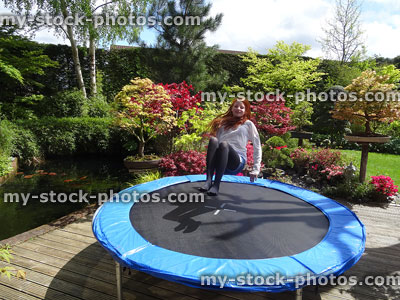 Stock image of girl doing sitting bounce, bouncing on garden trampoline