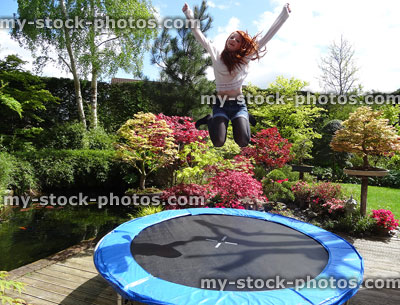 Stock image of girl jumping high on garden trampoline, no safety net