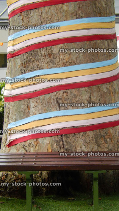 Stock image of London plane tree trunk decorated with ribbons, tree seat, artificial turf