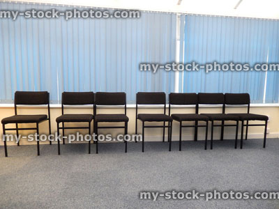 Stock image of doctor's waiting room, rows of black chairs, blue vertical blinds