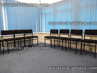 Stock image of doctor's waiting room, rows of black chairs, blue vertical blinds