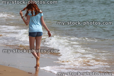 Stock image of girl walking barefoot on beach, sea waves, playing with hair