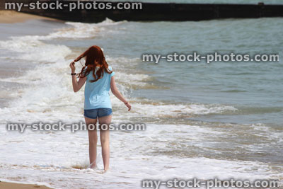 Stock image of girl walking barefoot on beach, sea waves, playing with hair