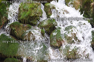 Stock image of natural waterfall splashing over mossy rocks, into river
