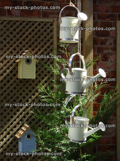 Stock image of small watering cans hanging by garden trellis / nest boxes