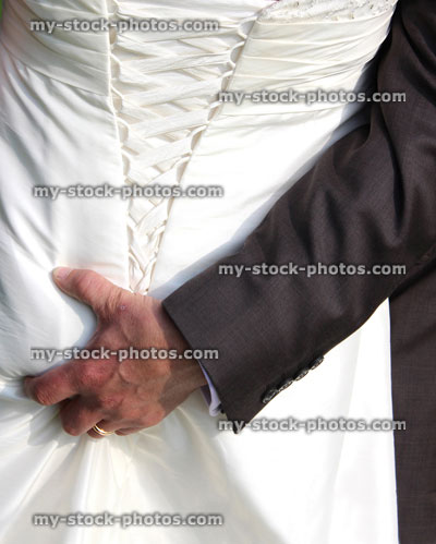 Stock image of bridegroom / groom squeezing bride's bottom, white wedding dress back detail