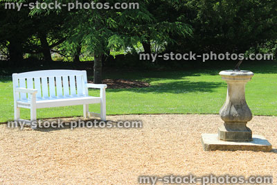 Stock image of wooden bench painted white with lawn, stone sundial