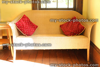 Stock image of wicker sofa / rattan loom style bench seat, red cushions, wooden floor