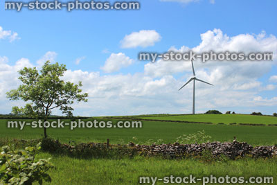 Stock image of wind turbine windmill in green field, blue sky, drystone wall