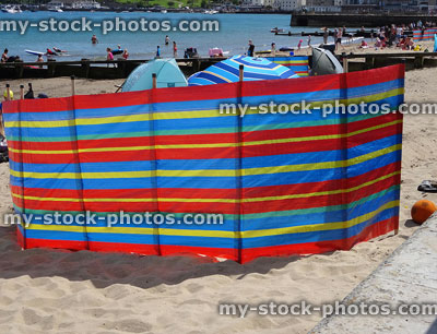 Stock image of colourful stripy windbreak at seaside beach with summer holidaymakers
