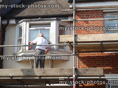 Stock image of handyman repairing rotten wooden windowframe on scaffolding platform