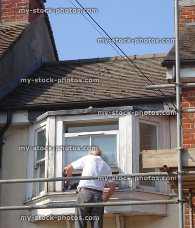 Stock image of builder repairing rotten wooden window frame on house