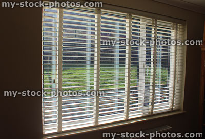 Stock image of white metal Venetian blind in window overlooking garden