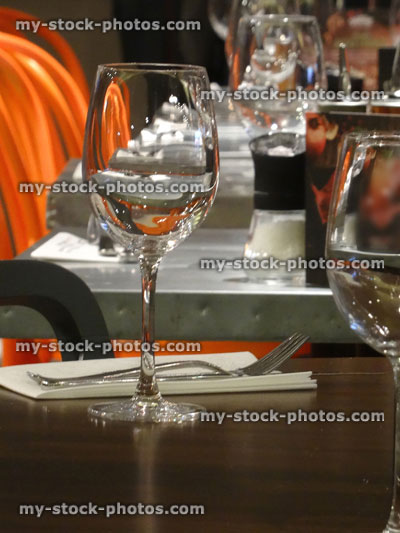Stock image of wooden restaurant tables with wine glasses, cutlery, serviettes / napkins, orange seats
