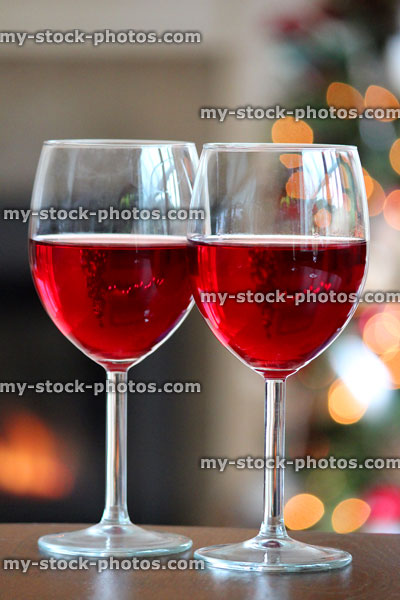 Stock image of red wine glasses with blurred Christmas fairylights, fireplace