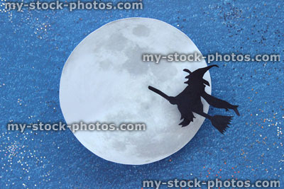 Stock image of black witch silhouette flying broomstick, paper moon, Halloween village / Halloween background