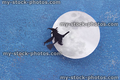 Stock image of black witch silhouette flying broomstick, paper moon, Halloween village / Halloween background