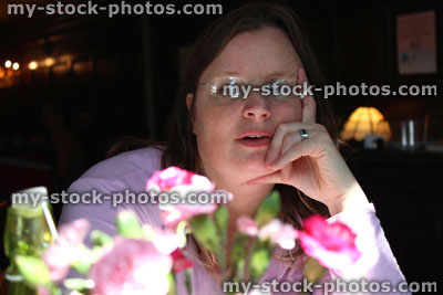Stock image of woman in restaurant, behind vase of flowers / carnations