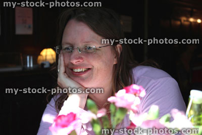 Stock image of woman in restaurant, behind vase of flowers / carnations