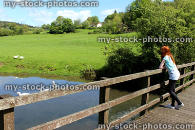 Stock image of girl standing on wooden bridge over river, watching ducks / geese