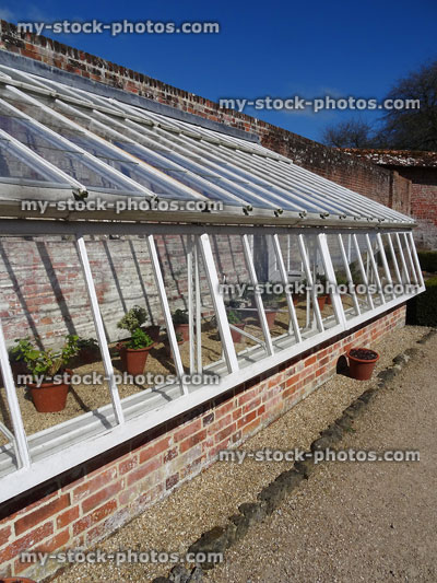 Stock image of white greenhouse / glasshouse in vegetable garden, red brick base