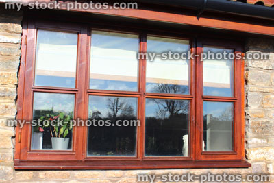 Stock image of double glazed varnished brown wooden window, glass panels, stone wall